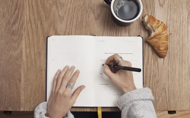 Persona anotando datos en un cuaderno sobre una mesa de madera